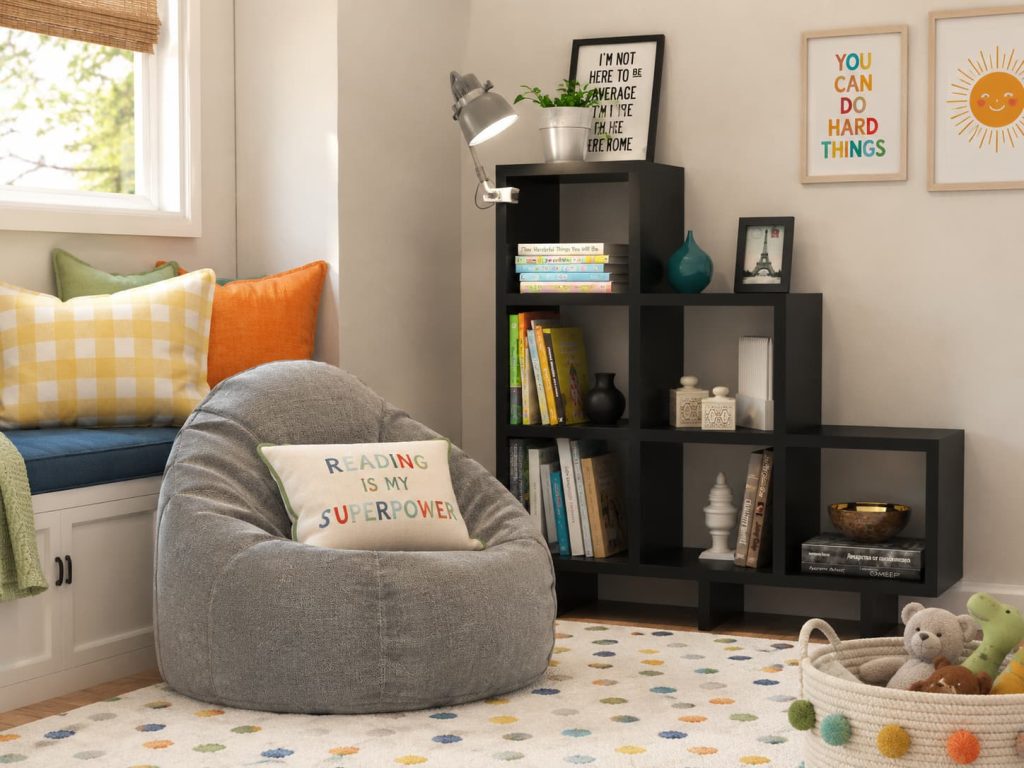 Children's reading nook with gray beanbag chair, tiered black bookshelf, window seat, and motivational wall art