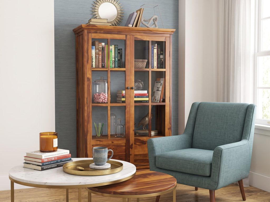 Coffee and books corner with a wood glass-door cabinet, a teal armchair, marble nesting tables, and a gold tray
